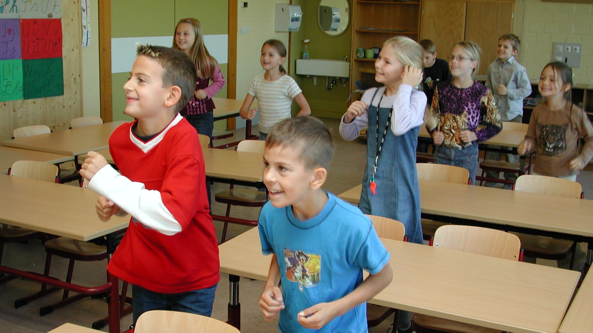 Kinder stehen an ihrem Platz im Klassenraum, zu den Informationen für Schulen.