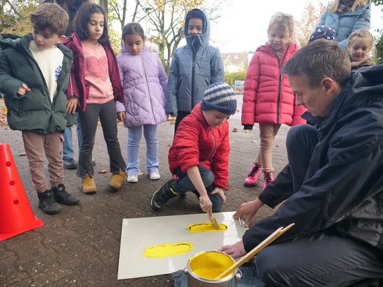 Schülerinnen und Schüler malen mithilfe ihres Lehrers Gelbe Füße auf die Straße.